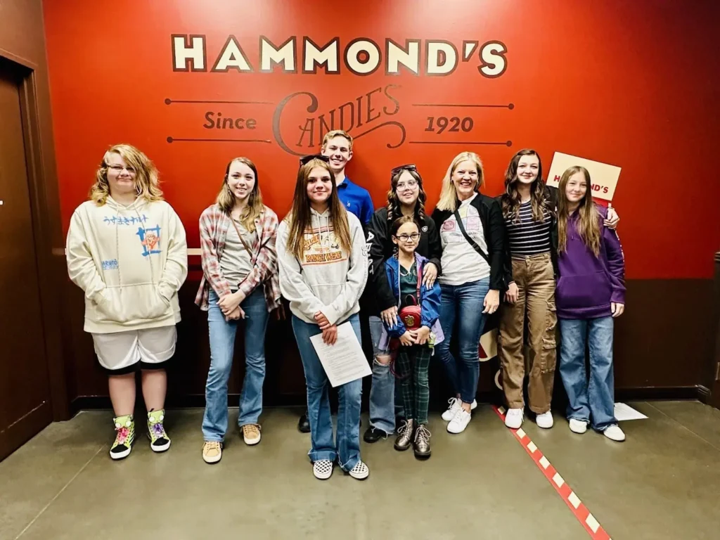 Group of people posing in front of the Hammond's Candies sign, established 1920.