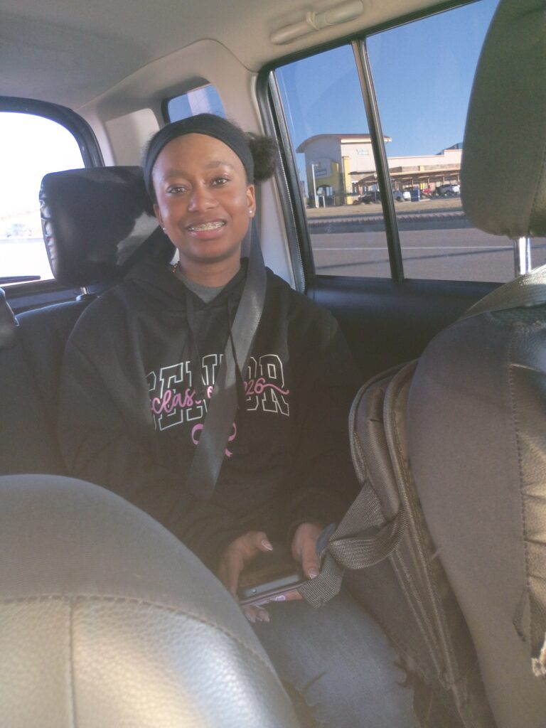 A person sits in the back seat of a car wearing a seatbelt and holding a phone.