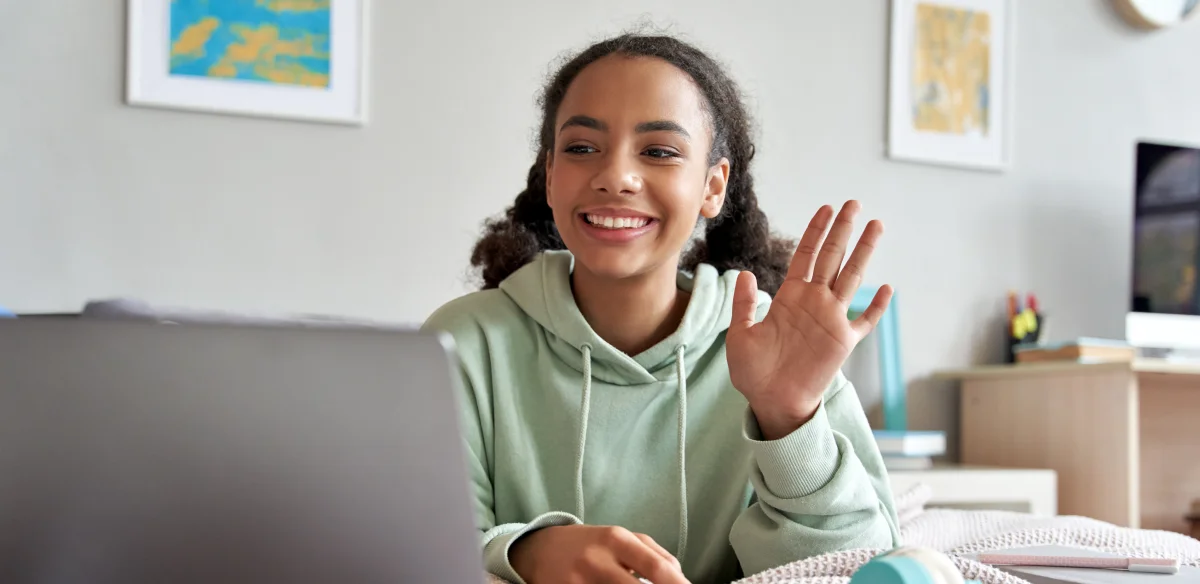 High school student waiving at her online class wearing a light green hoodie