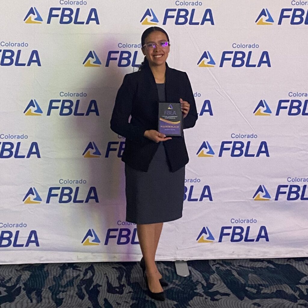 Person standing in front of a Colorado FBLA banner, holding a trophy and smiling.