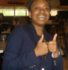 Person in a navy blazer giving two thumbs up in an indoor cafeteria setting.