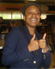 Person in a navy blazer giving two thumbs up in an indoor cafeteria setting.