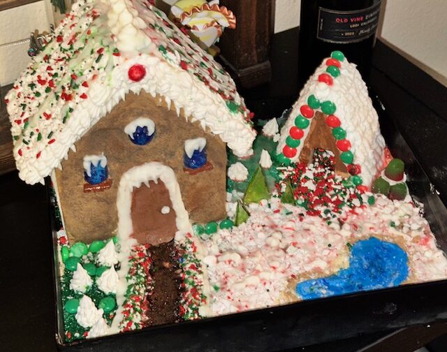 A decorated gingerbread house displayed on a tray with icing, candy details, and a snowy holiday theme.